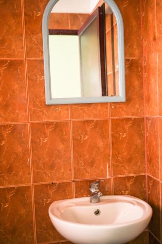 a bathroom sink with a mirror on a tiled wall at Hotel Xhejsoni in Shëngjin