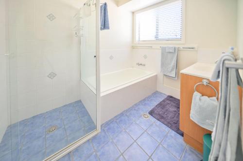 a bathroom with a tub and a shower with blue tiles at Lomandra in Evans Head