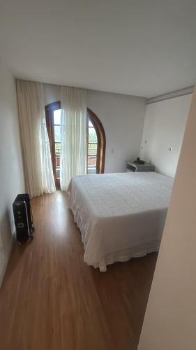 a bedroom with a white bed and a window at Quatre Saisons Residence Apartamentos Duplex com linda vista em Campos do Jordão in Campos do Jordão