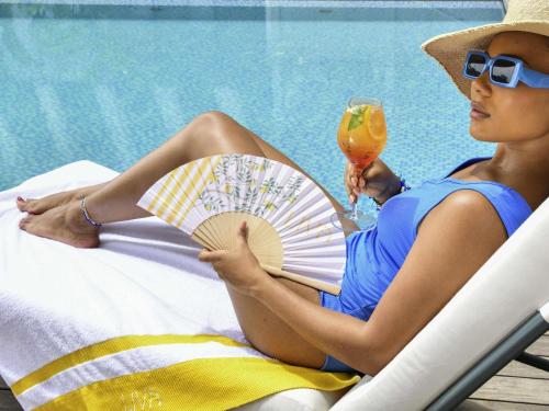 a woman sitting in a chair holding a fan and a drink at Novotel Abidjan Marcory in Abidjan