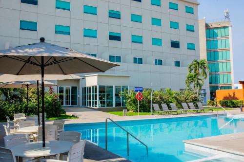 a pool with chairs and an umbrella next to a building at Holiday Inn Express Manzanillo by IHG in Manzanillo