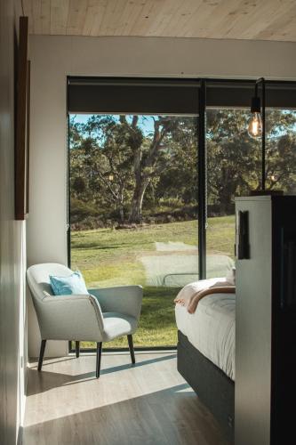 a bedroom with a bed and a chair and a window at Softfoot Farm Luxury Retreats in Hindmarsh Valley