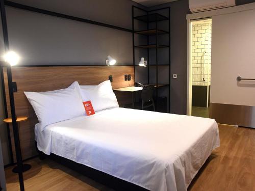a bedroom with a white bed with a red tag on it at ibis Tangará Da Serra in Tangara da Serra