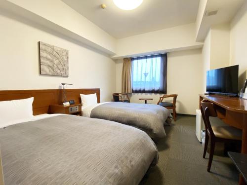 a hotel room with two beds and a desk at Hotel Route-Inn Mojiko in Kitakyushu
