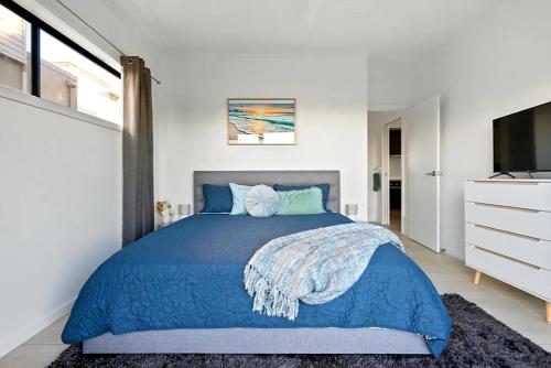 a bedroom with a blue bed and a television at Surfside Getaway Caves Beach Absolute Beachfront in Caves Beach
