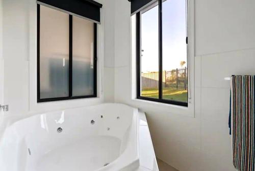 a white bathroom with a tub and two windows at Surfside Getaway Caves Beach Absolute Beachfront in Caves Beach