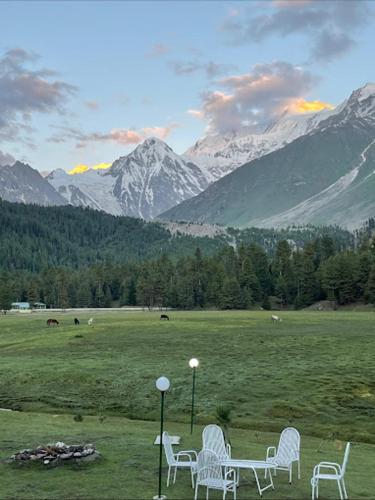 a group of white chairs in a field with mountains at Rama lake view Hotel in Astor