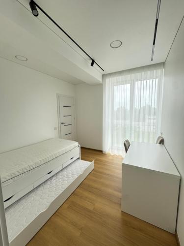 a white bedroom with a bed and a desk at River View Apartment in the Park in Marijampolė