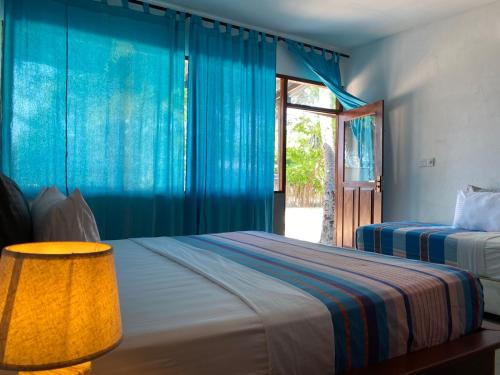 a bedroom with two beds with blue curtains and a window at Vibration Nilaveli in Trincomalee