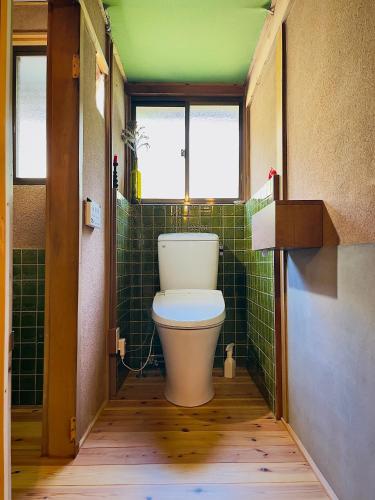 a bathroom with a toilet in a room with green tiles at Homestay HANIHOHETO in Ena