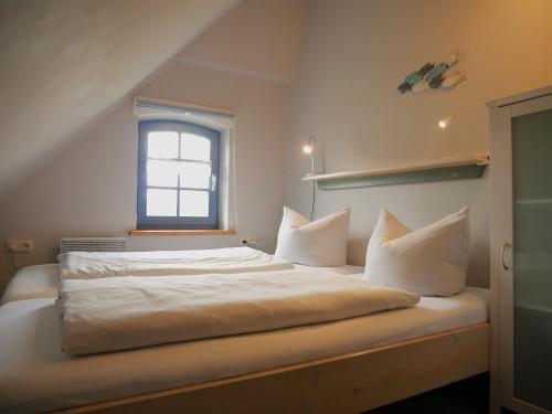 a bedroom with a bed with white sheets and a window at Poeler Inselhaus in Kaltenhof