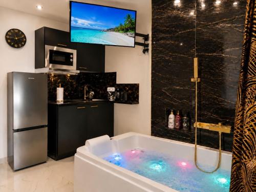 a bathroom with a tub with a tv and a kitchen at Luxury Beach Room in Frontignan