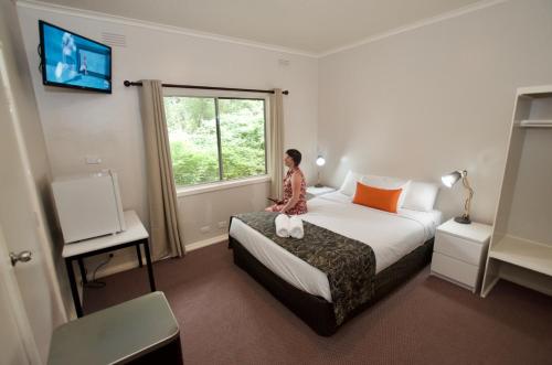 una mujer sentada en una cama en una habitación de hotel en Mountain View Holiday Retreat, en Harrietville