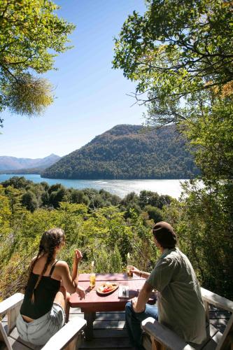two people sitting at a picnic table with a view of a lake at Hermoso Eco Lodge in San Martín de los Andes