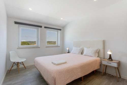 a white bedroom with a bed and two windows at Casa "O Chafariz" in Amoreira