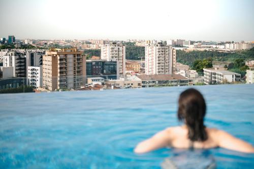 a woman in a swimming pool looking at a city at Jupiter Porto Hotel - Rooftop & Spa in Porto