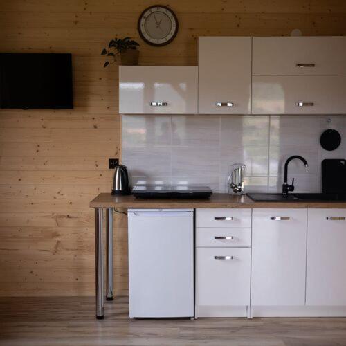 a kitchen with white cabinets and a clock on the wall at Domki Lawendowa Skarpa in Zawóz