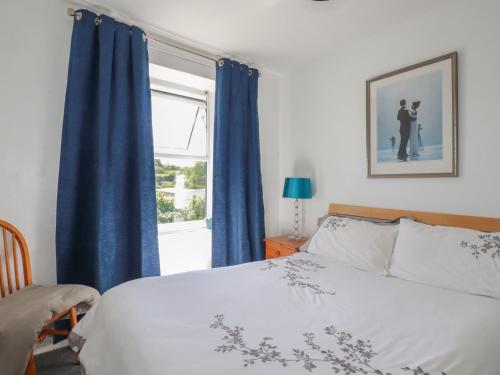a bedroom with a bed with blue curtains and a window at Tin Lantern Cottage in Redruth