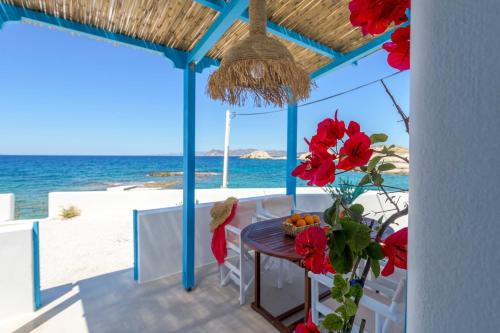 a table with red flowers on a balcony with the beach at Esperanza Home Mandrakia in Mandrakia