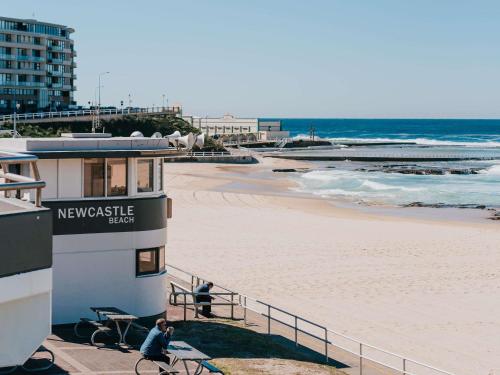 two people riding bikes on the beach next to a building at Novotel Newcastle Beach in Newcastle