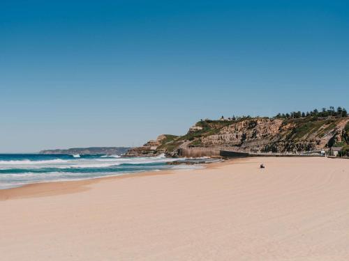 a sandy beach with a person sitting on the beach at Novotel Newcastle Beach in Newcastle