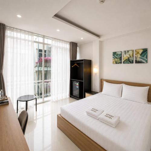 a bedroom with a large white bed with a table and a chair at Atusy Hotel in Ho Chi Minh City