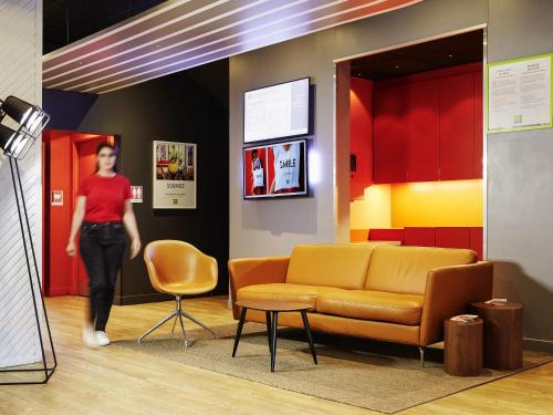 a woman walking through a waiting room with a couch at Ibis Styles Paris Massena Olympiades in Paris