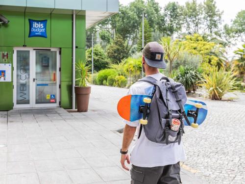 a man with a backpack and a skateboard in front of a building at Hotel ibis Budget Porto Gaia in Vila Nova de Gaia