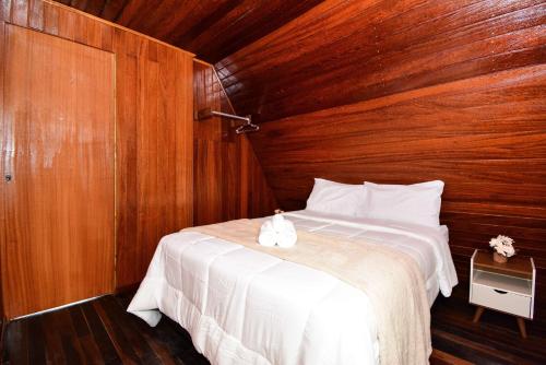 a bedroom with a white bed with wooden walls at Chalé com Jacuzzi e Vista Mar - PLH007 in Palhoça