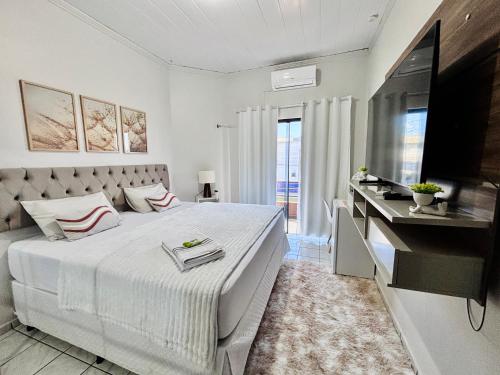 a white bedroom with a large bed and a television at Hospedagem Domiciliar em Lucas do Rio Verde in Lucas do Rio Verde