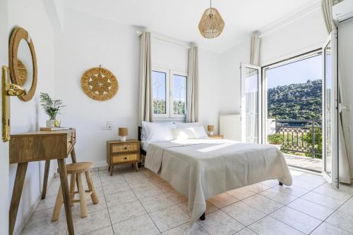 a white bedroom with a bed and a large window at Casa Mia Skopelos - Spacious 3-Bedroom House near Stafylos Beach in Skopelos Town