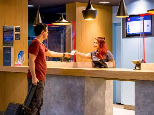 a man and a woman shaking hands at a counter at ibis Marilia in Marília