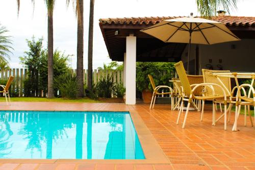 a patio with a table and an umbrella next to a pool at Hotel Residence Jaguary in Jaguariúna