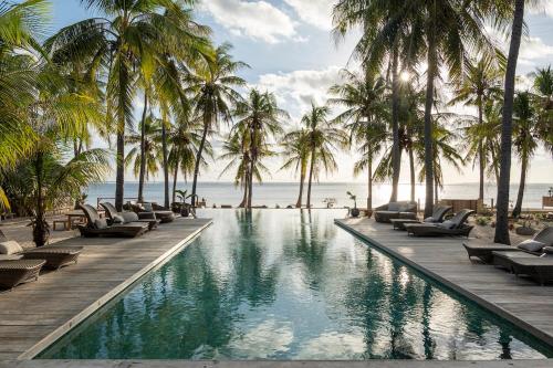 a pool at the beach with palm trees and chaise lounges at Seed Resort in Nembrala