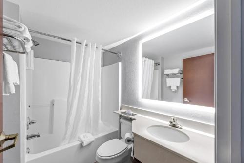 a bathroom with a sink and a toilet and a mirror at Clarion Pointe Starkville near University in Starkville