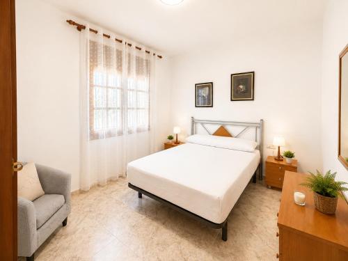 a white bedroom with a bed and a chair at AmetllaDeMar in Les tres Cales