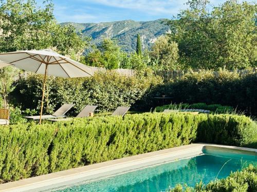 a swimming pool with an umbrella and two chairs and a table with an umbrella at La Villa Bohème Piscine Jardin Vue Luberon in Oppède