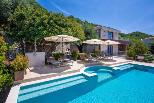 a swimming pool with chairs and umbrellas next to a house at Villa Svinjista in Budva