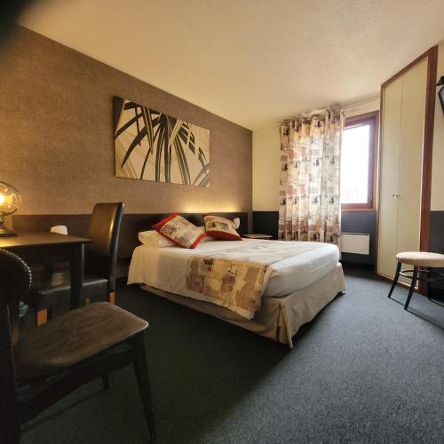 a bedroom with a bed and a table and a window at Logis Hôtel Le Merle Blanc in Digoin