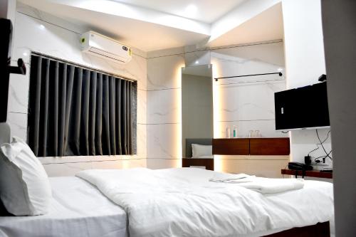 a bedroom with a white bed and a television at Infinity Hotel in Rajkot