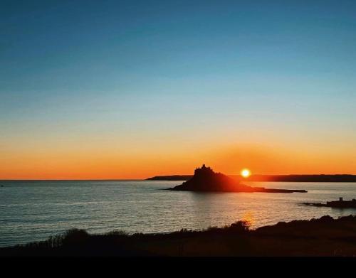 a sunset over the ocean with a castle on an island at Spacious Studio by the sea, Garden & Parking in Marazion