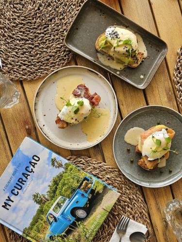 three plates of food on a table with a book at Yucca mini boutique hotel - Adults only in Jan Thiel