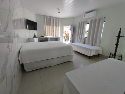 a white bedroom with two beds and a table at Quarto Califórnia in Campo Novo do Parecis