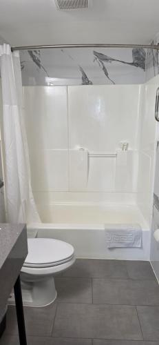a white bathroom with a toilet and a bath tub at South Bay Motel in Copiague