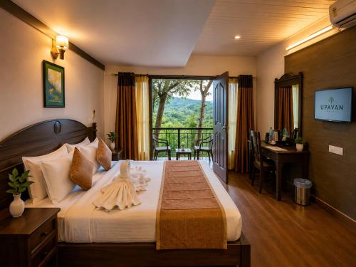 a bedroom with a bed with a desk and a balcony at Upavan Resort in Vythiri