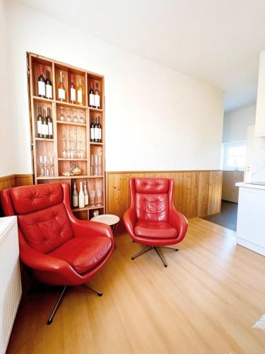 two red chairs in a room with a shelf of wine bottles at Apartment by the lake in Píšťany