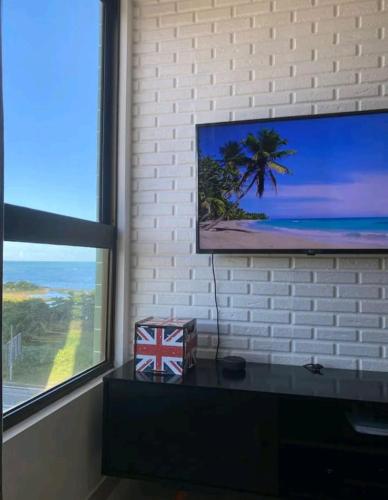 a television on a brick wall with a table with a box at Apt Completo com Vista para o Mar, Ar Condicionado e Café da Manhã Opcional in Recife
