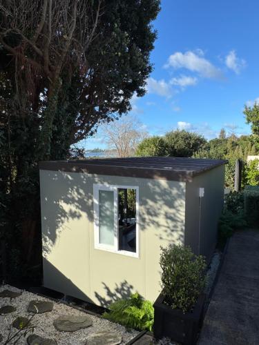 a small shed with a window in a garden at Pōhutukawa Studio in Tauranga