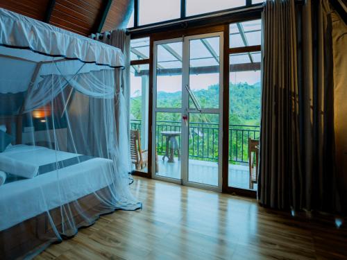 a bedroom with a bed and a balcony with glass doors at Haven Crest Sinharaja in Deniyaya