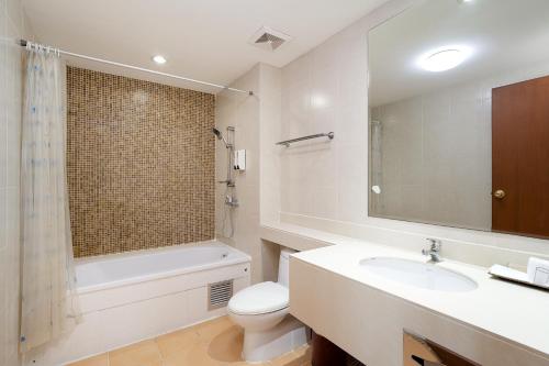 a bathroom with a sink and a toilet and a mirror at Lasalle Suites Hotel & Residence in Bangkok